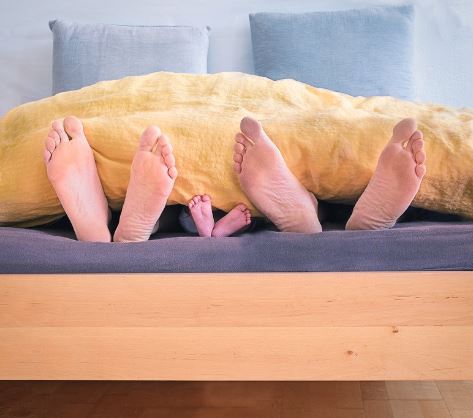 family-of-three-lying-on-bed-showing-feet-while-covered-with-blanket